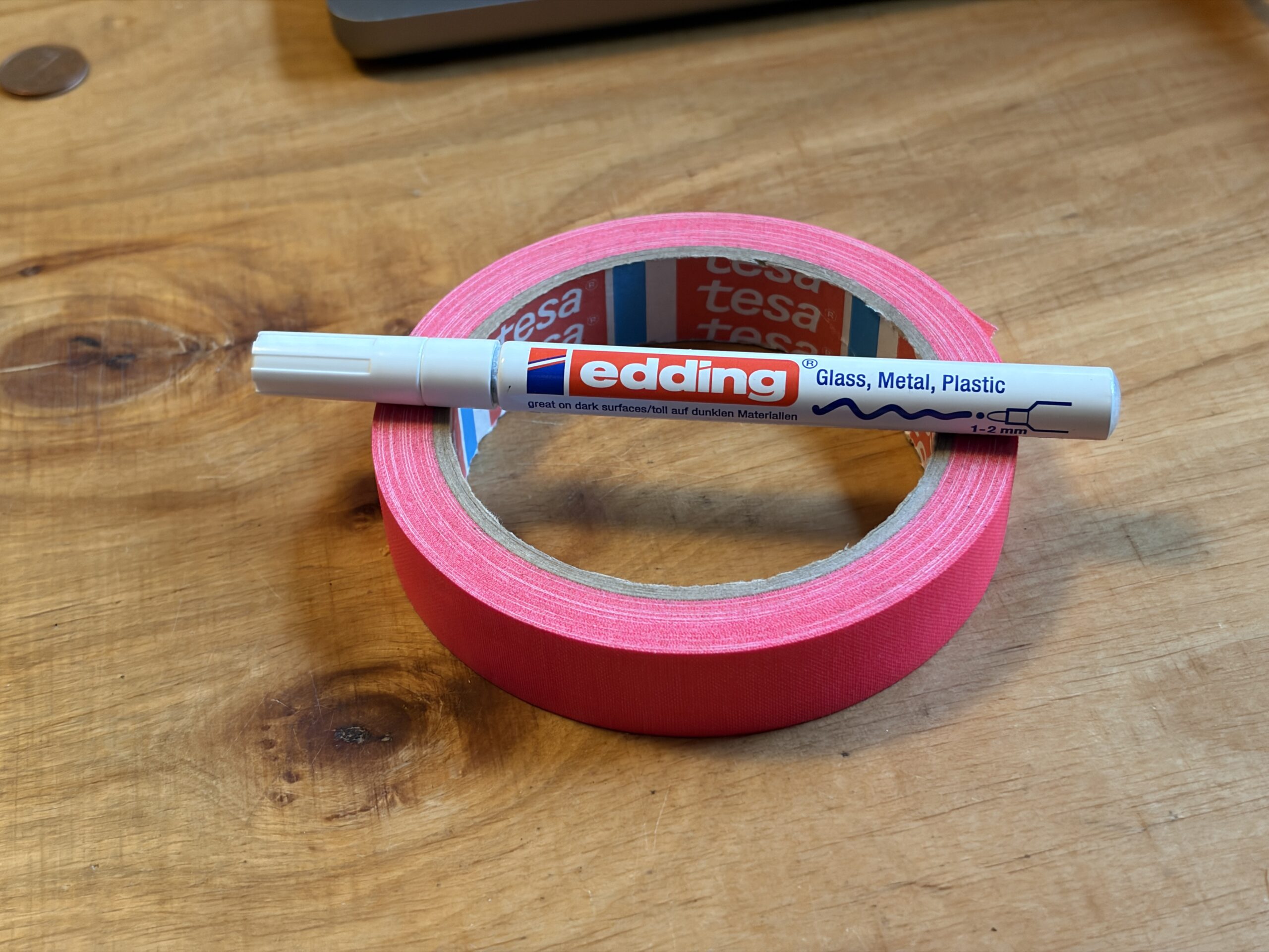 Weißer Edding auf einer Rolle pinkem Tesa-Gewebeband auf einem Holztisch